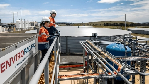 Two engineers in hi-vis gear on a walkway above an Enviropacific treatment facility and large storage tanks
