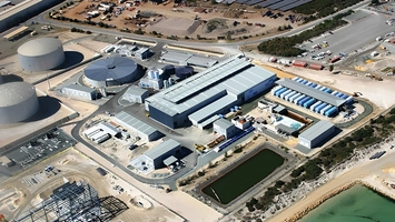 Aerial view of a large coastal water treatment plant with circular tanks and blue processing buildings