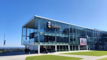 Modern glass-facade Flinders University building with branded signage and crest set against a clear blue sky
